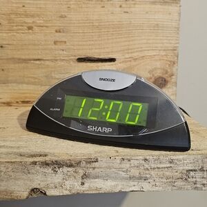 Sharp digital alarm clock featuring a green LED display, a top snooze button